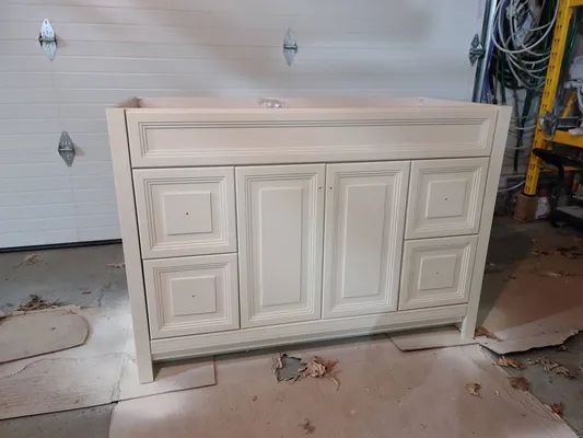 Cream-colored bathroom vanity with two sets of drawers and two doors, set in a garage with a closed garage door.