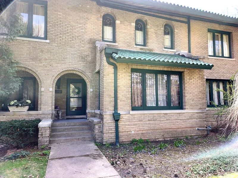 Two-story brick house with green trim and a tiled overhang. The front door is arched and has steps.