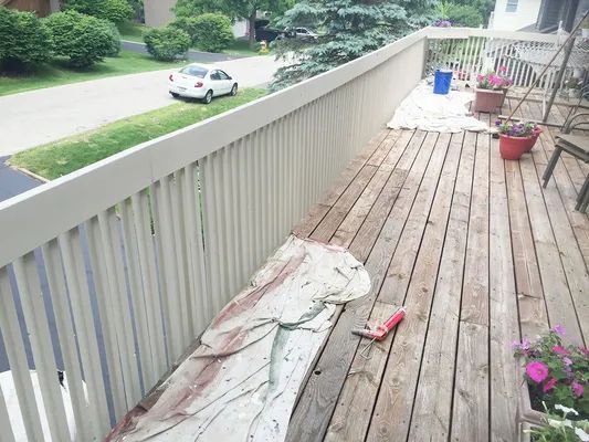 Wooden deck with white railing; car and street visible in background.