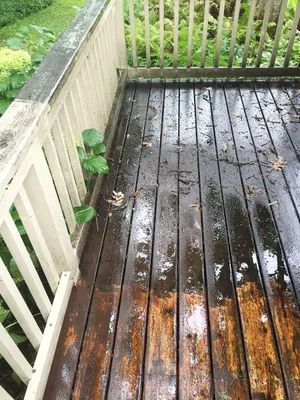 Partially cleaned wooden deck with brown boards and white railing.