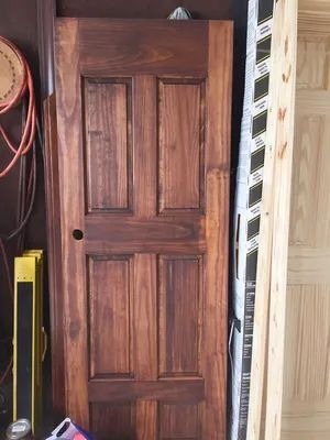 Brown stained wooden door with four panels, leaning against a wall.