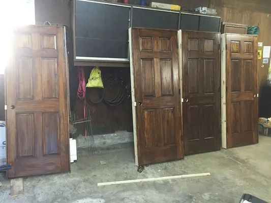 Four wooden doors of varying shades leaning against a wall in a garage.