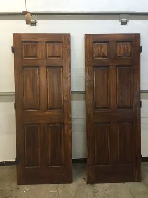 Two wooden doors, stained brown, lean against a white wall. They have a classic six-panel design.