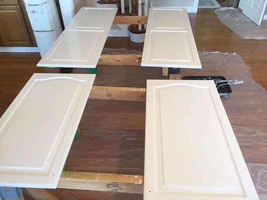 Four off-white cabinet doors laid out for painting on a wooden table in a home.