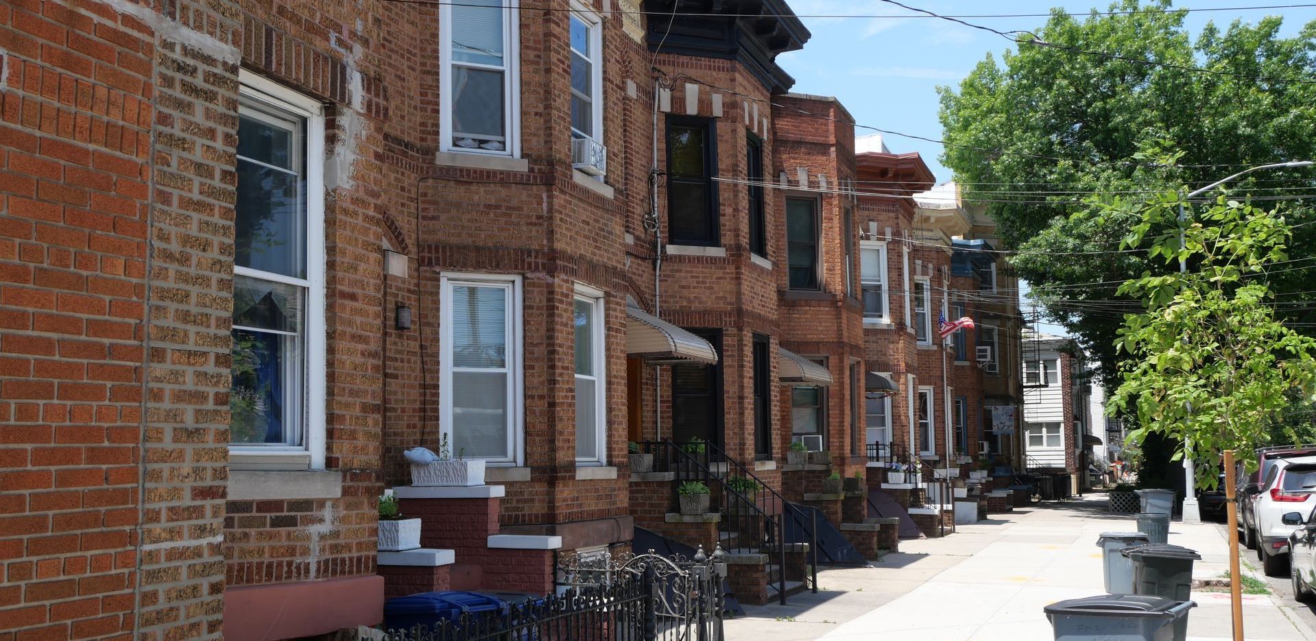 A row of brick houses in Ridgewood Queens are lined up on a city street.