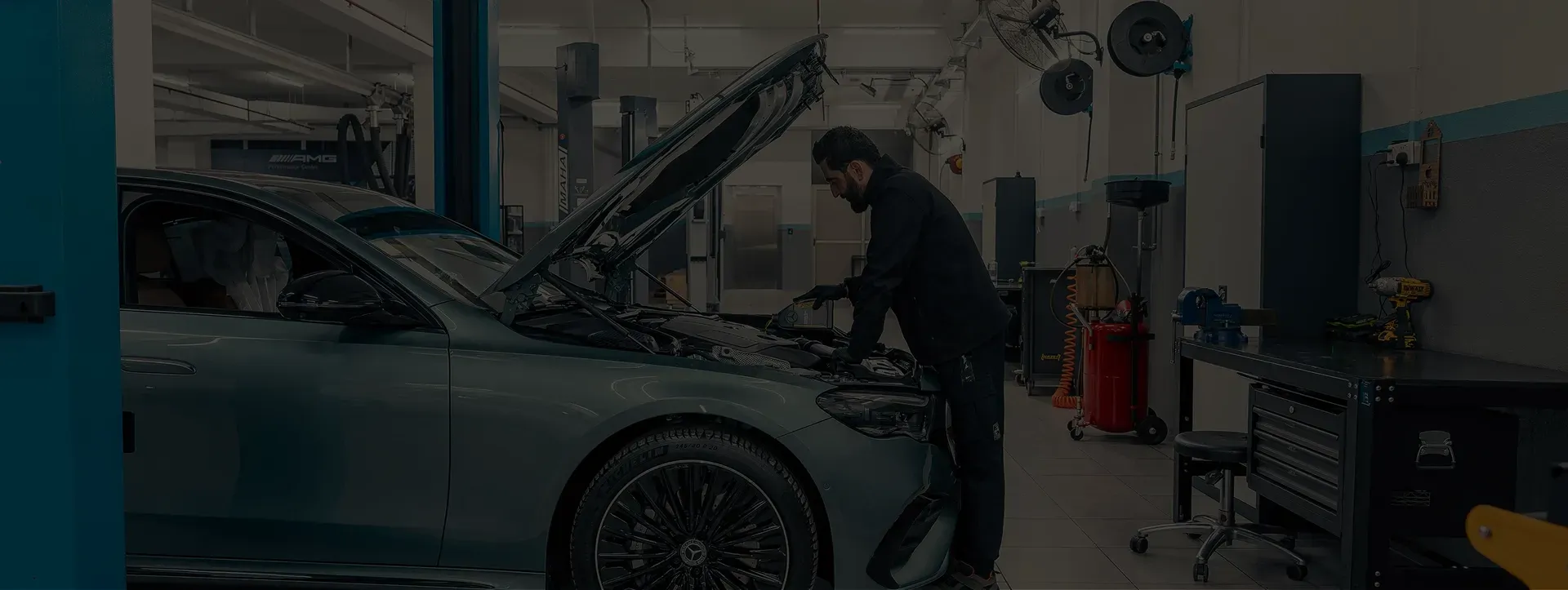 Technician inside garage looking inside hood of light blue car | Autohaus Merkle