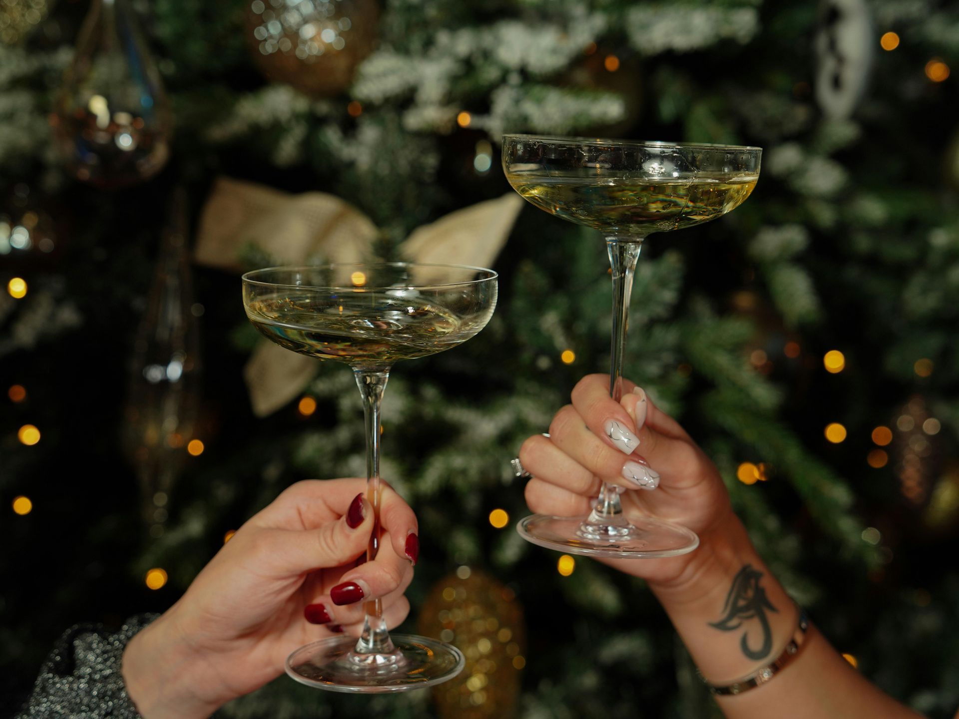 Two people are toasting with champagne glasses in front of a christmas tree.