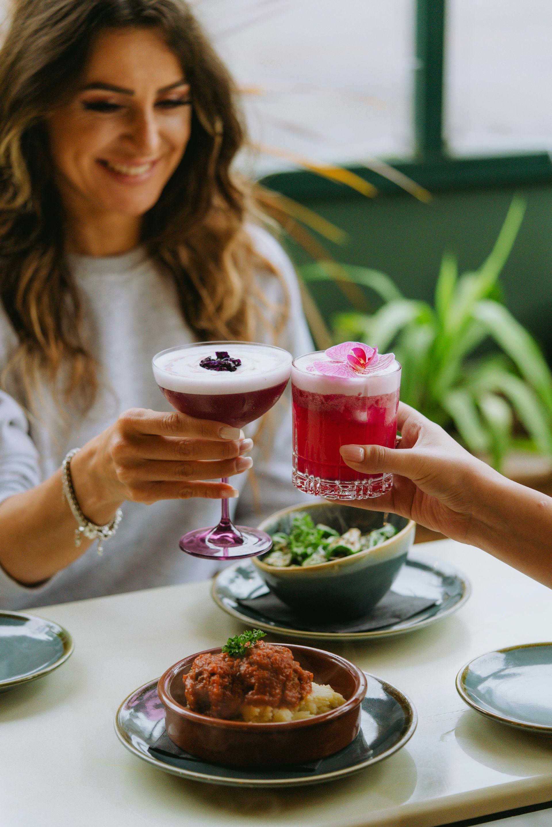 A woman is sitting at a table with plates of food and drinks.