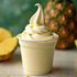 Pineapple Dole Whip in a cup with fresh pineapple and a pineapple in the background.