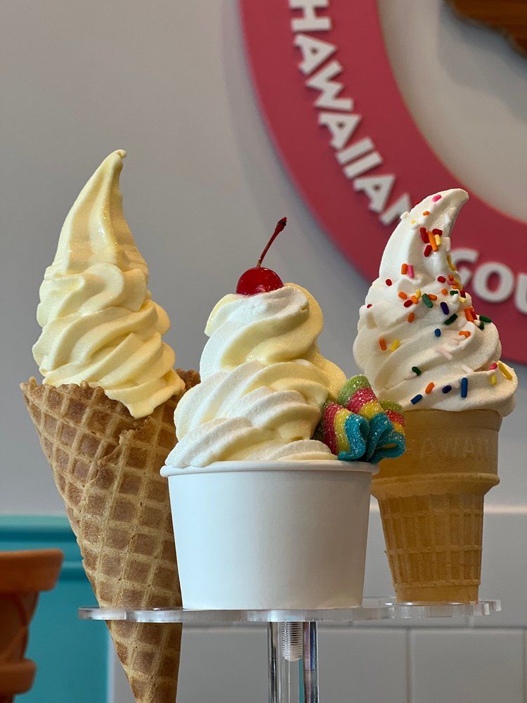 Three soft serve ice cream treats: waffle cone, cup with cherry, and cone with sprinkles.