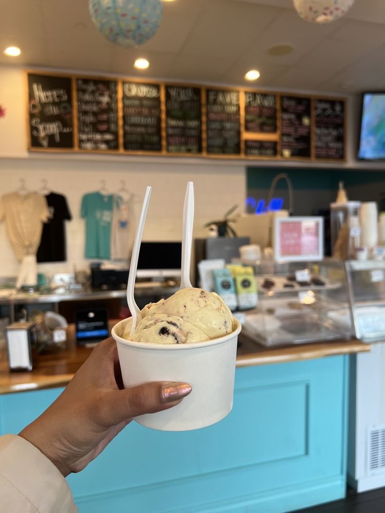 Person holding ice cream cup in an ice cream shop. Scoops of ice cream, blue and white decor.