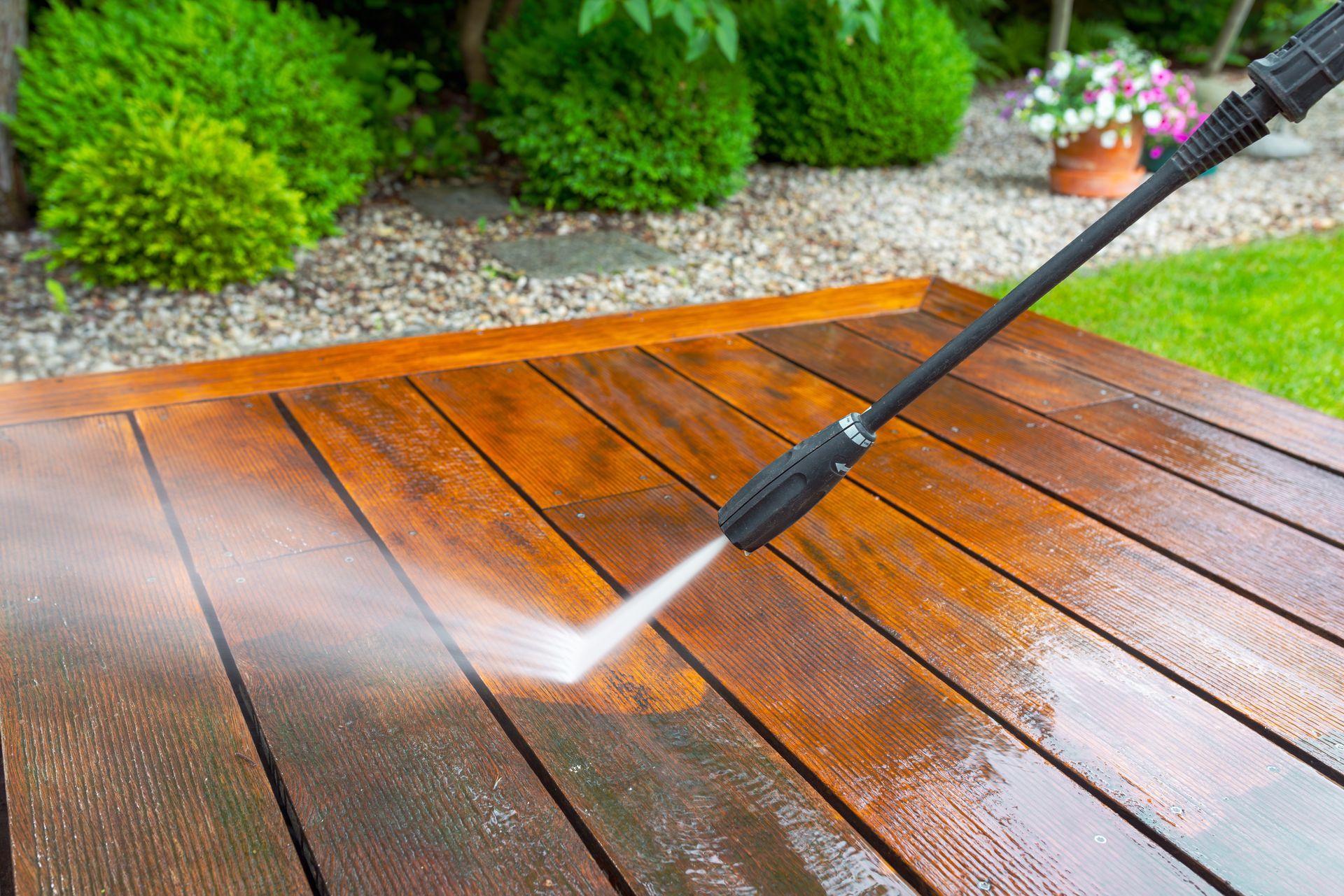 A person is using a high pressure washer to clean a wooden deck.