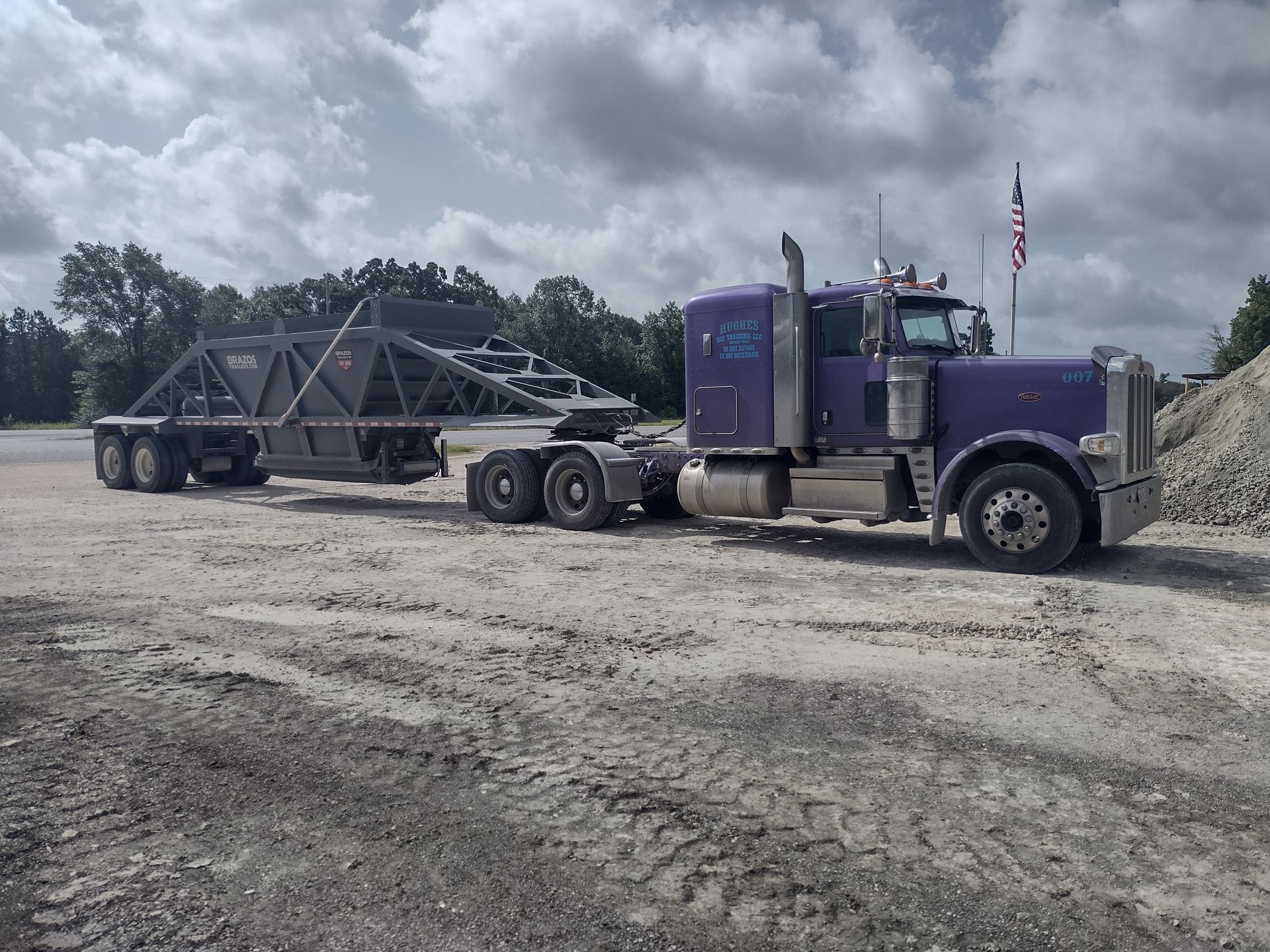 A purple semi truck is parked in a dirt lot