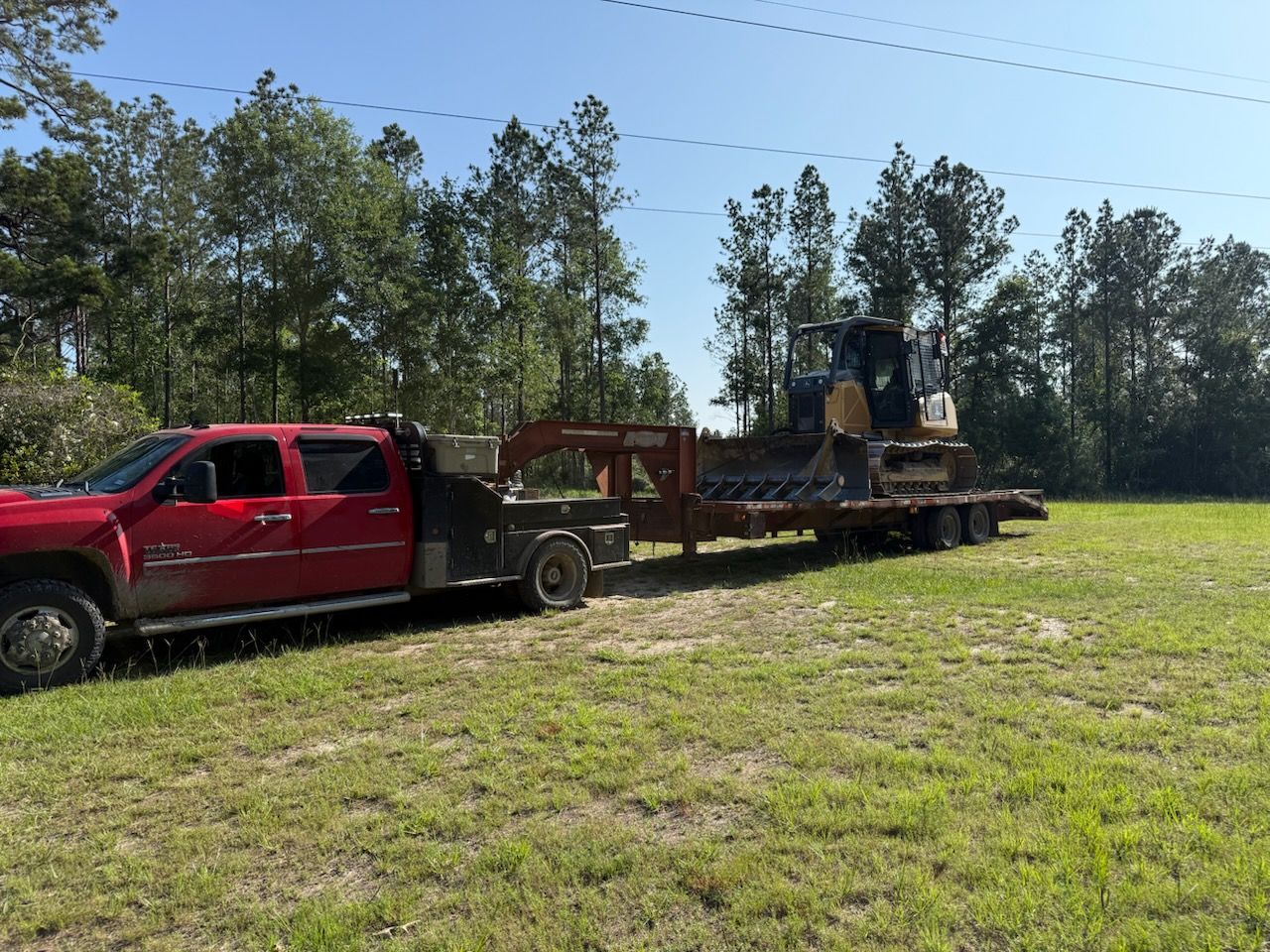 A red truck is towing a bulldozer on a trailer.