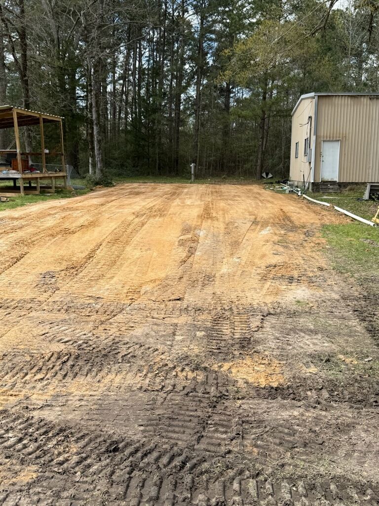 A dirt road with a building in the background and trees in the background.