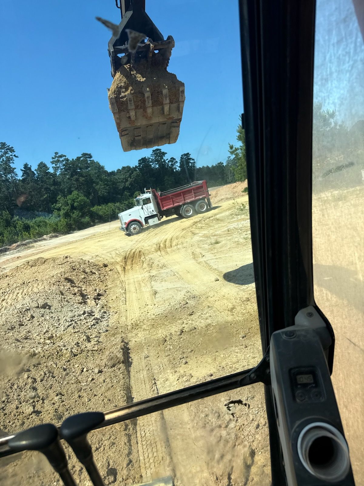 A dump truck is being loaded with dirt by a crane.