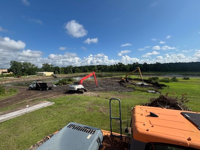 A large orange excavator is sitting in the middle of a grassy field.
