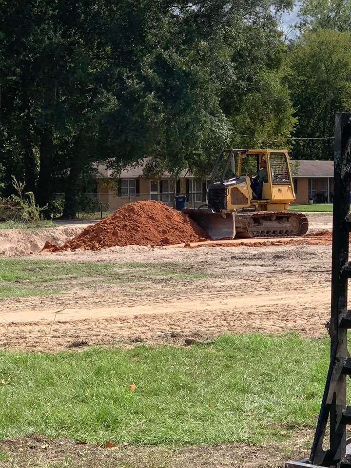A bulldozer is moving dirt in a field near a house