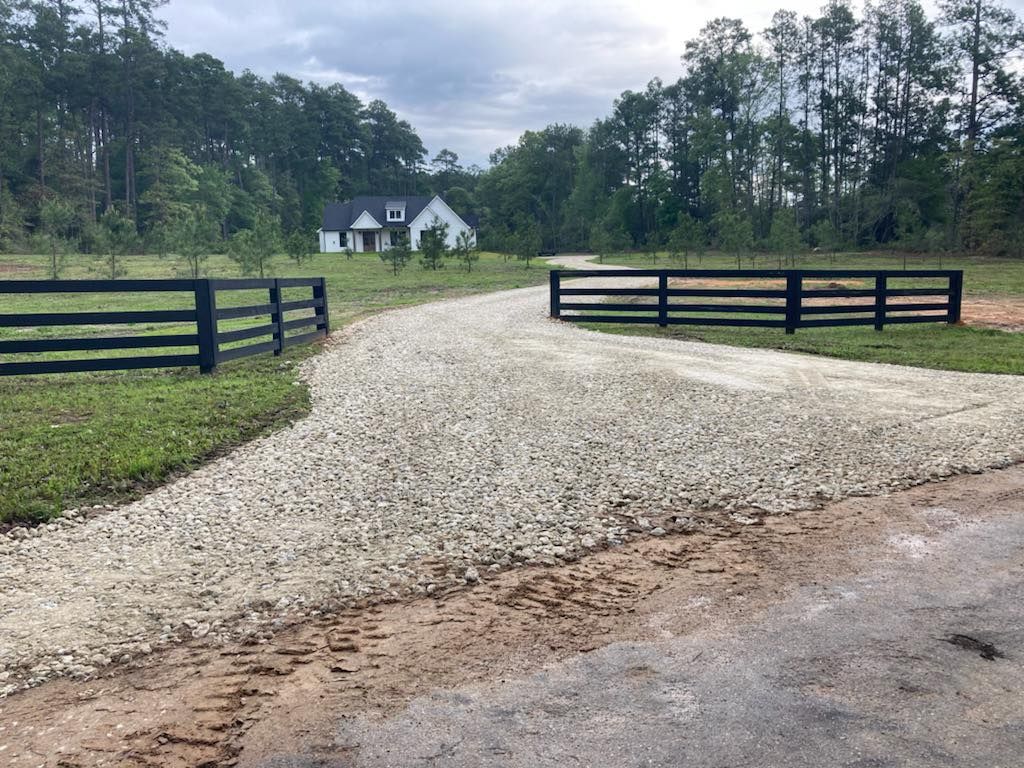 A gravel road leading to a house with a wooden fence.