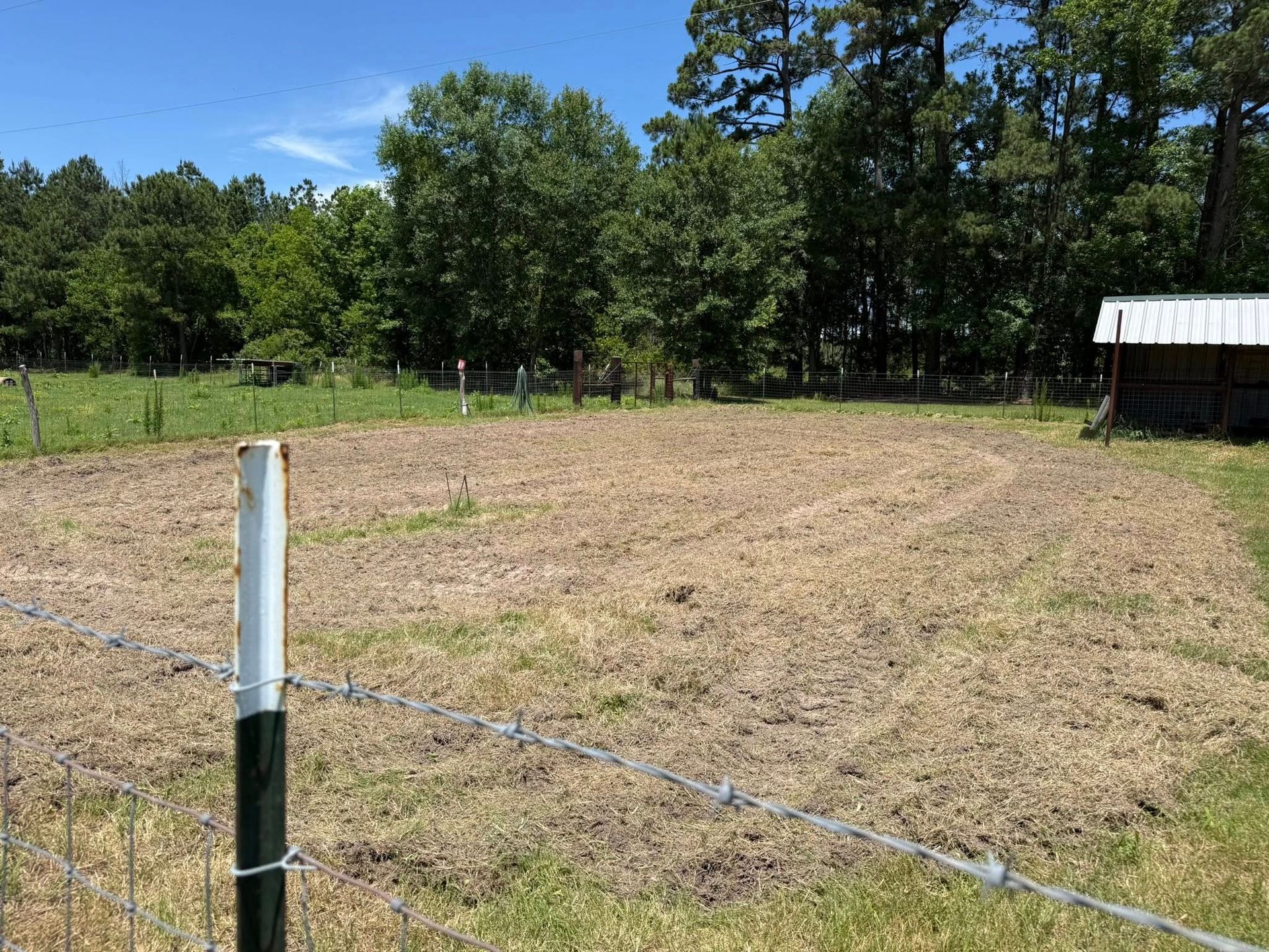 A barbed wire fence surrounds a field with trees in the background.