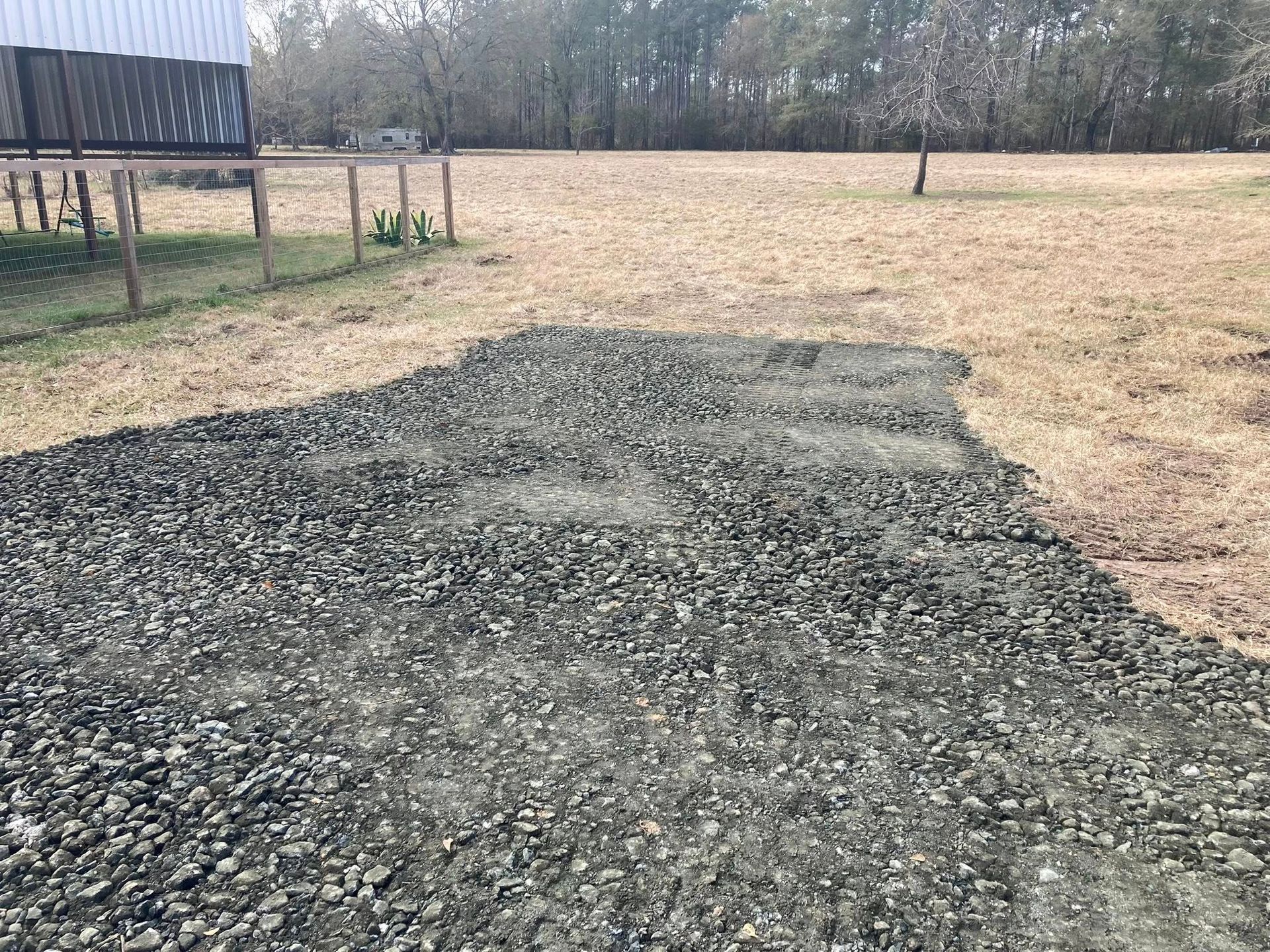 A gravel driveway in a field with a barn in the background.
