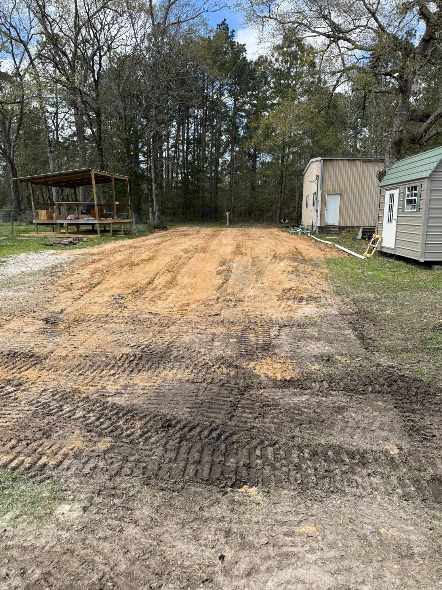 A dirt road with a shed in the background and trees in the background.