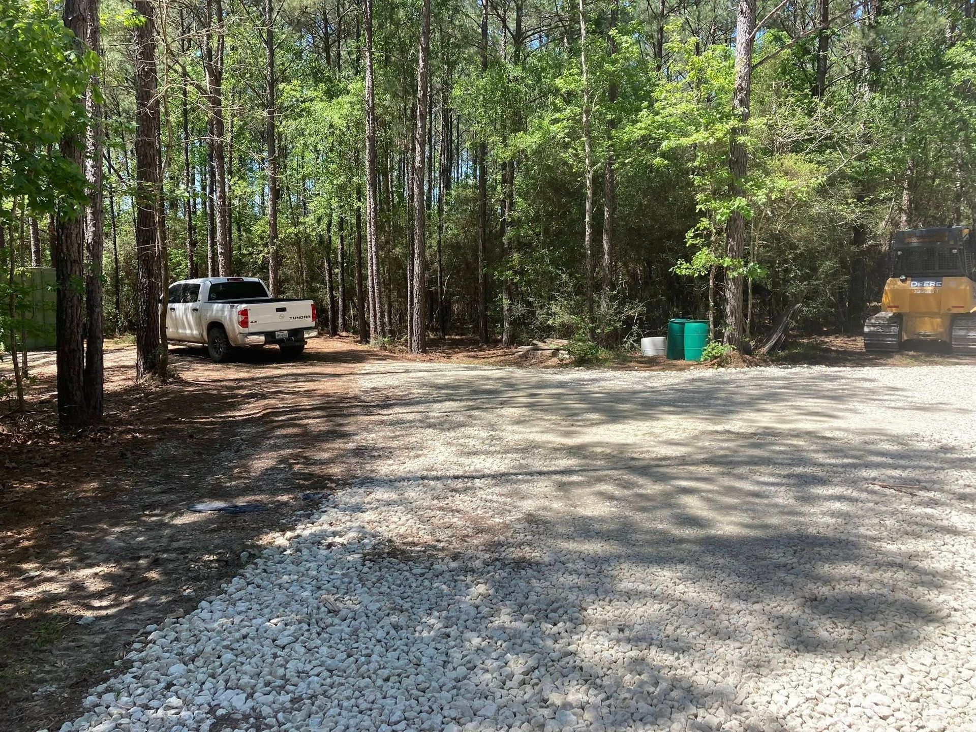 A white truck is parked in a gravel lot in the middle of a forest.