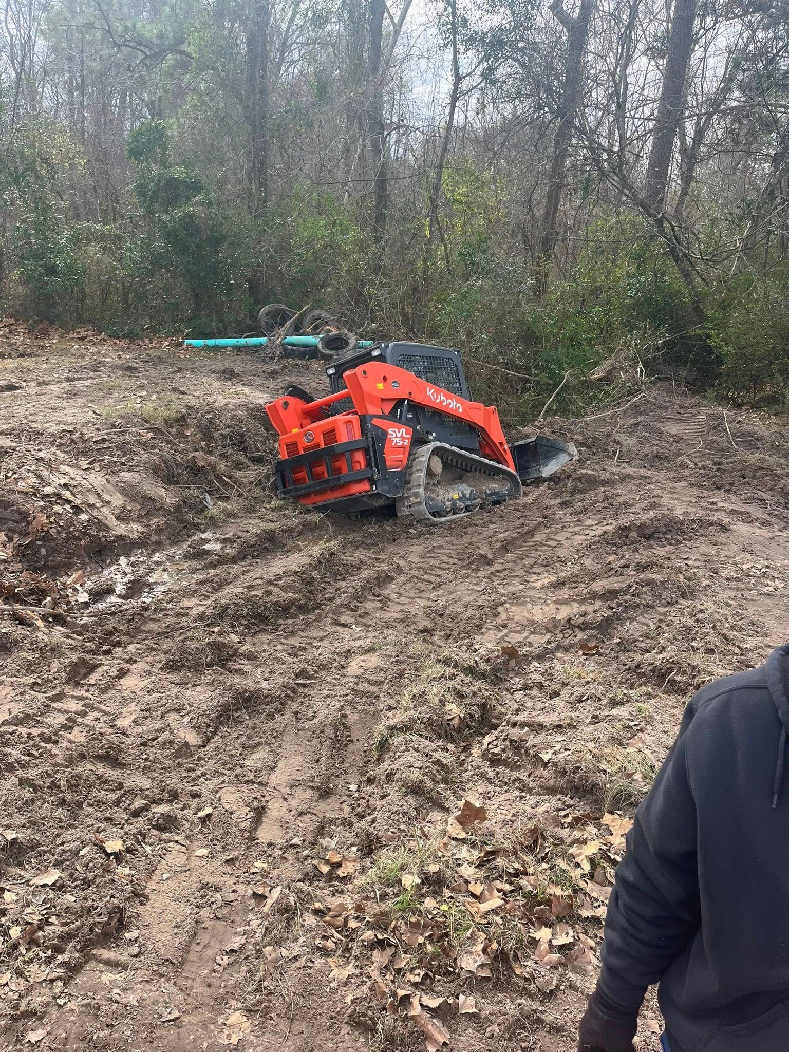 A man is standing next to a tractor that is stuck in the mud.