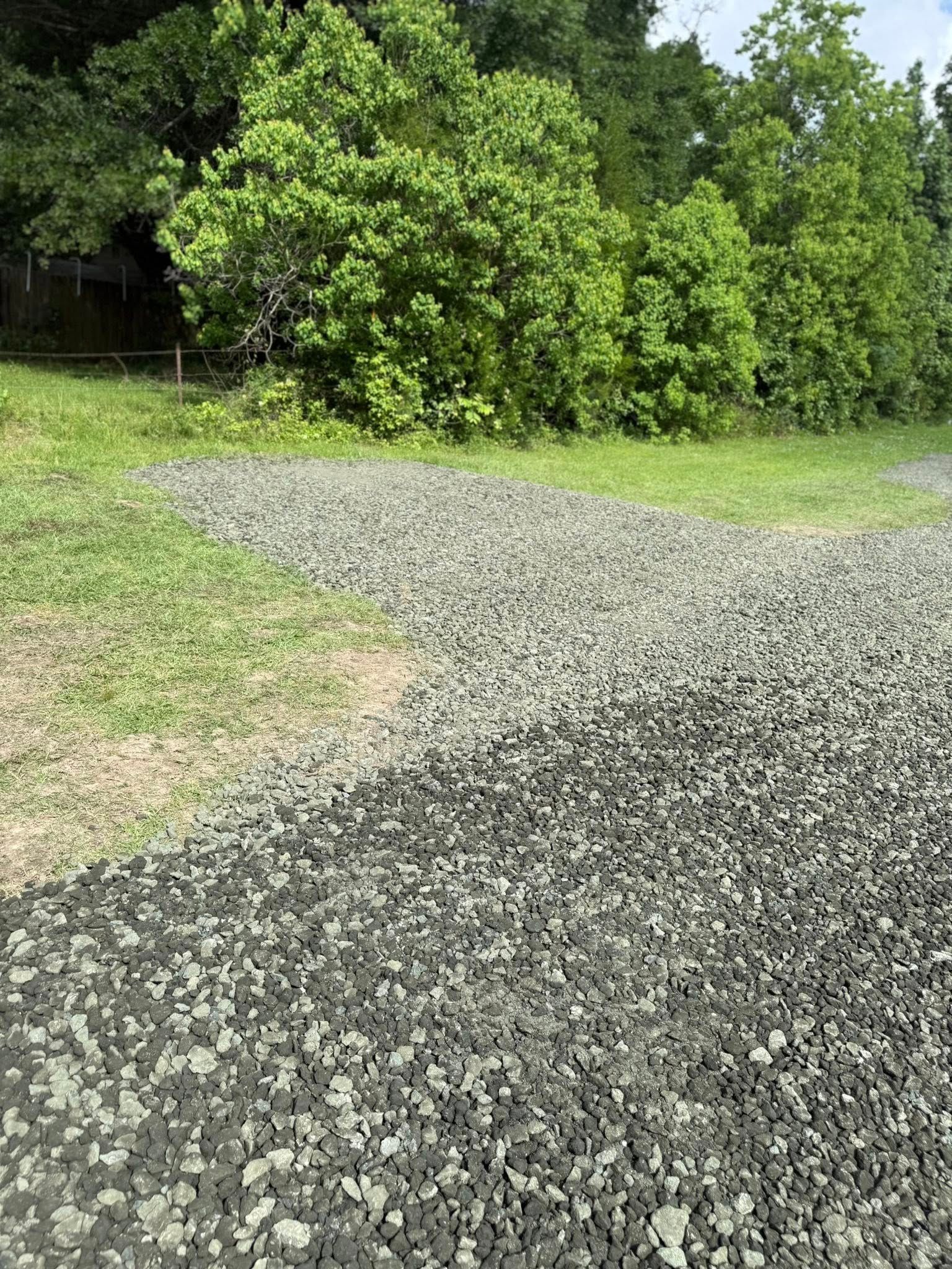 A gravel road leading to a grassy field with trees in the background.