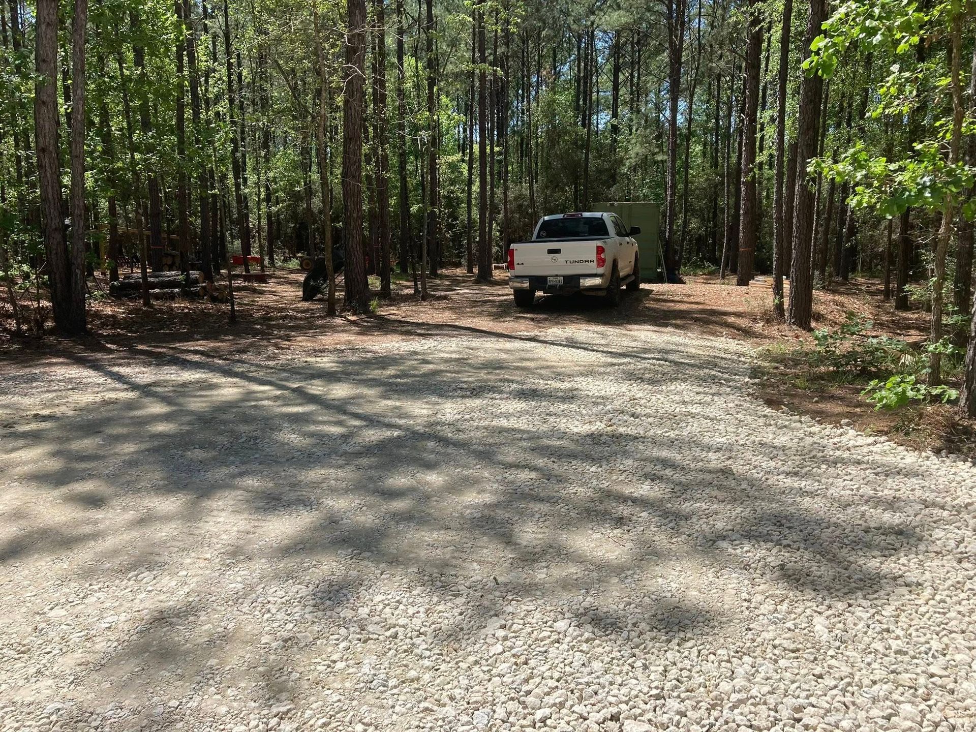 A white truck is parked on a gravel road in the woods.