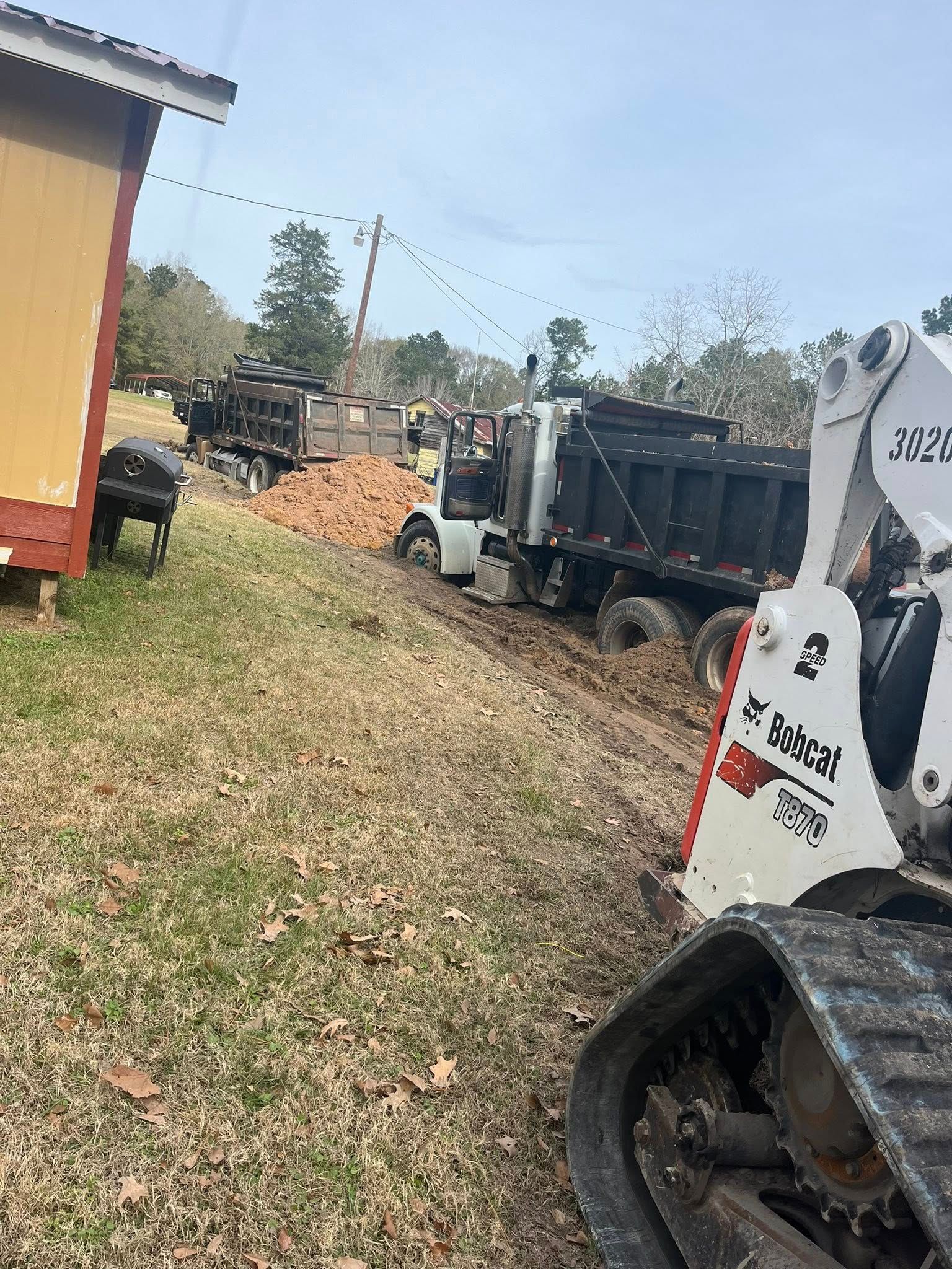 A bulldozer is driving down a dirt road next to a dump truck.