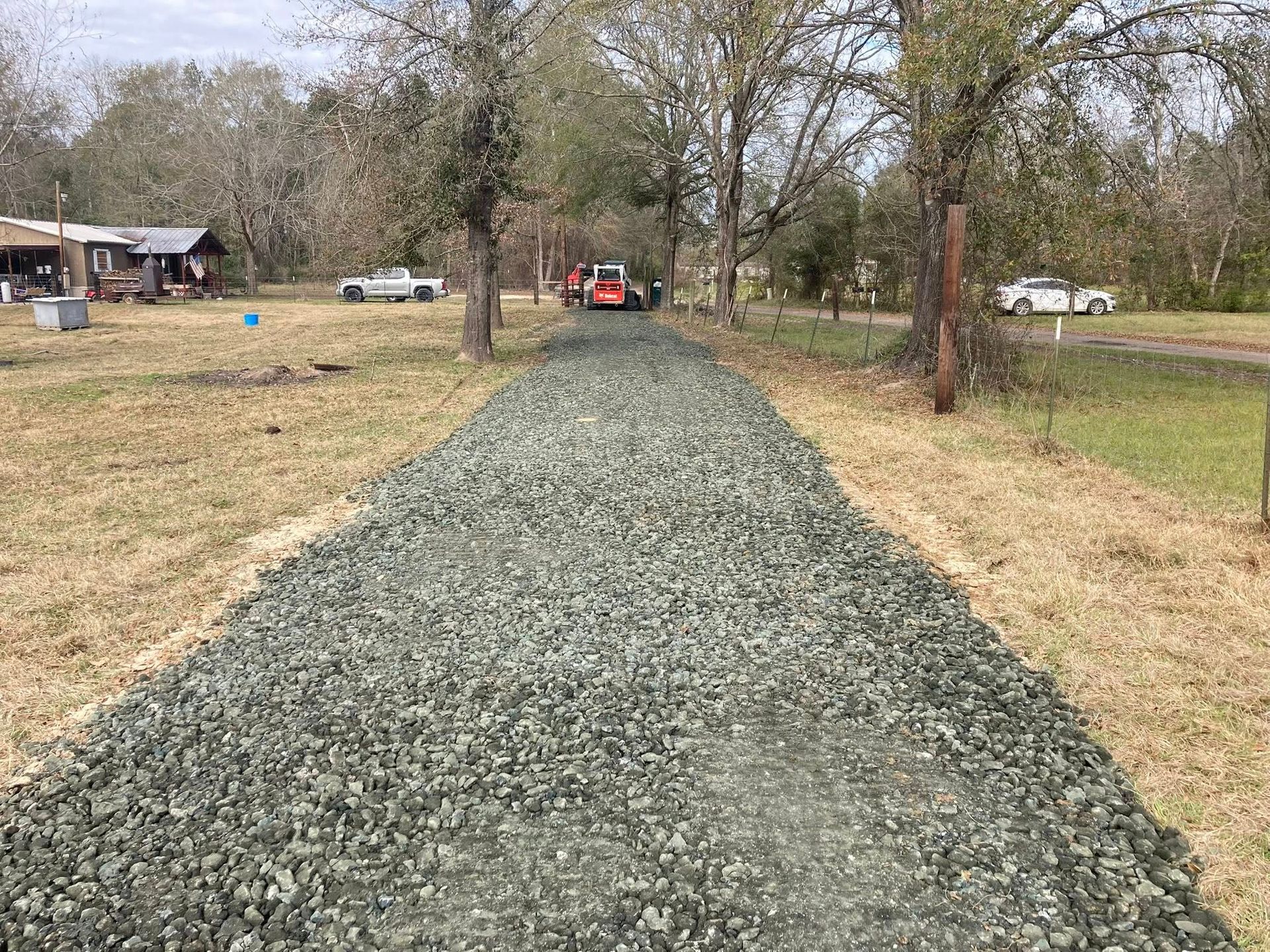 A gravel road going through a field with a house in the background.