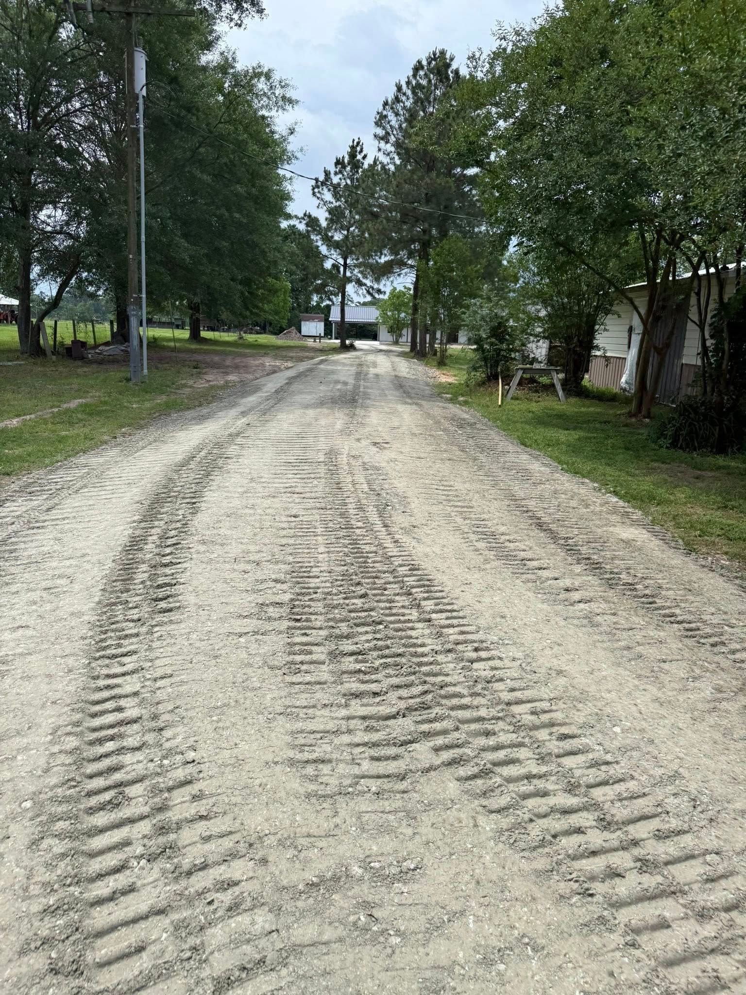A dirt road leading to a house with trees on both sides.