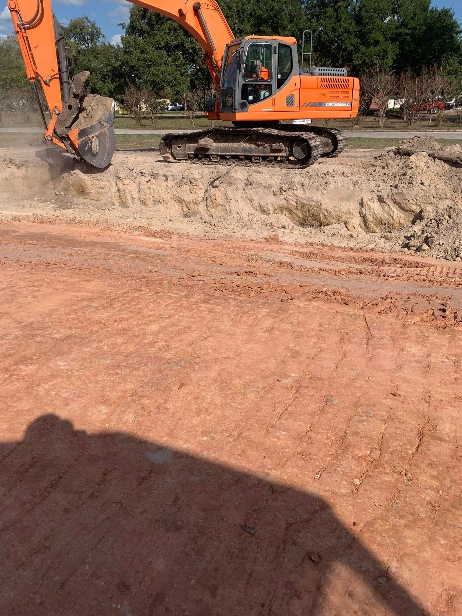 A large orange excavator is digging a hole in a dirt field.