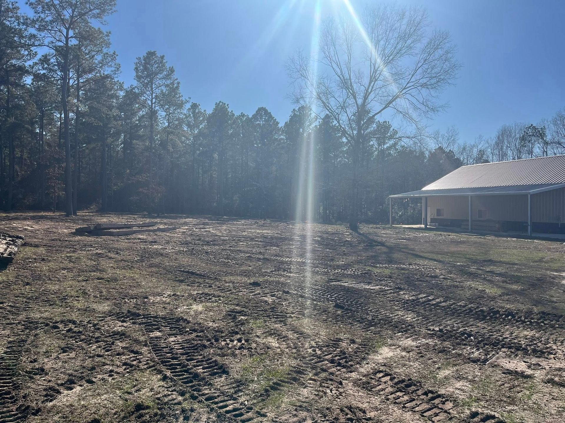 A house is sitting in the middle of a dirt field surrounded by trees.