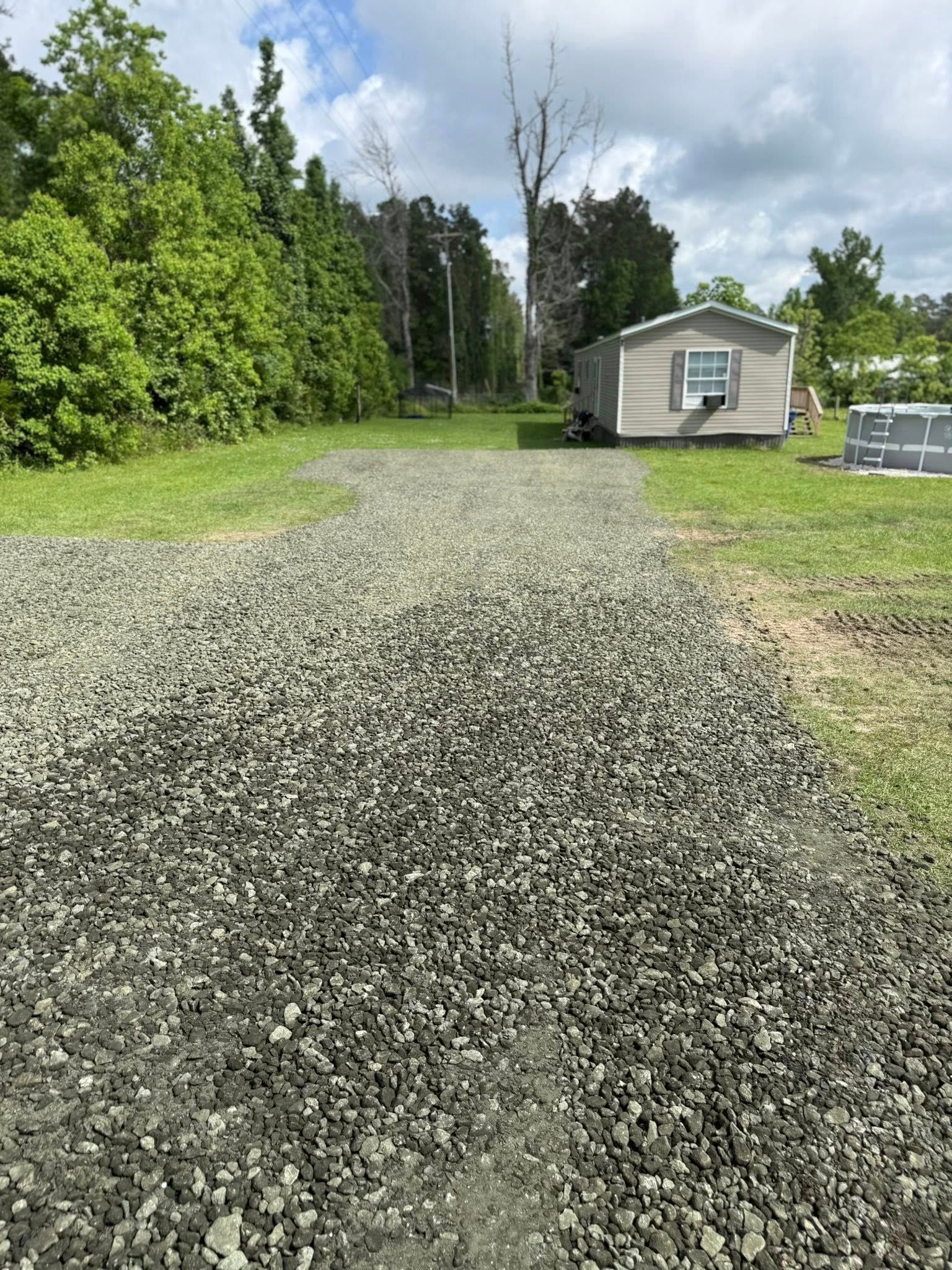 A gravel driveway leading to a mobile home in the middle of a grassy field.