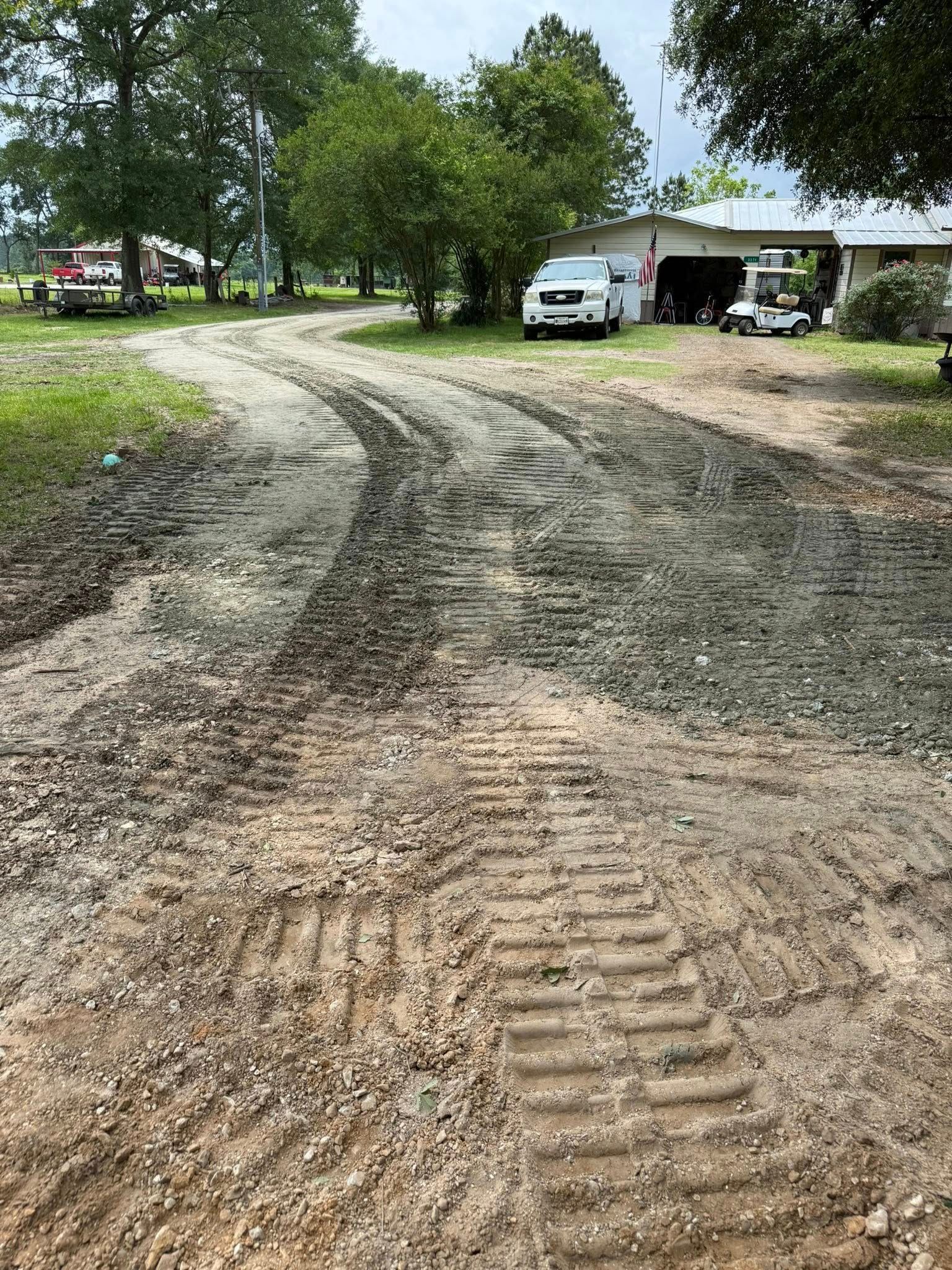A dirt road leading to a house with cars parked on the side of it.