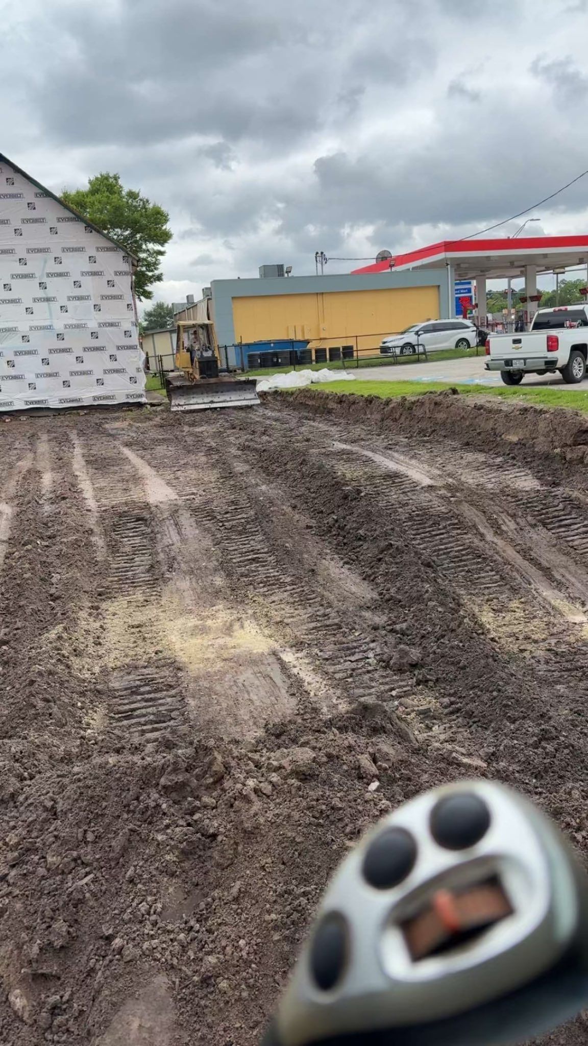 A person is measuring a dirt field in front of a gas station.