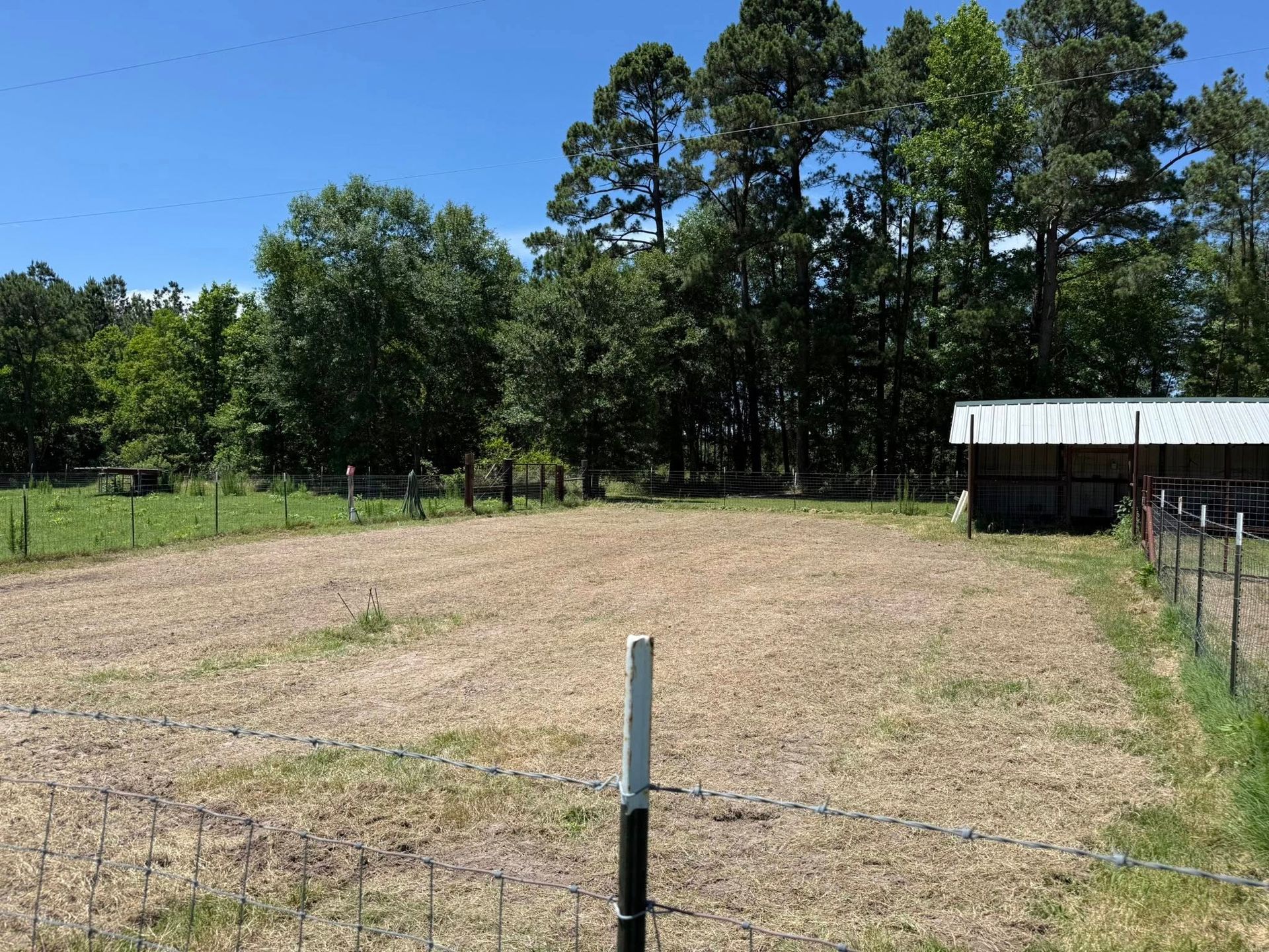 A dirt field with a fence and trees in the background.