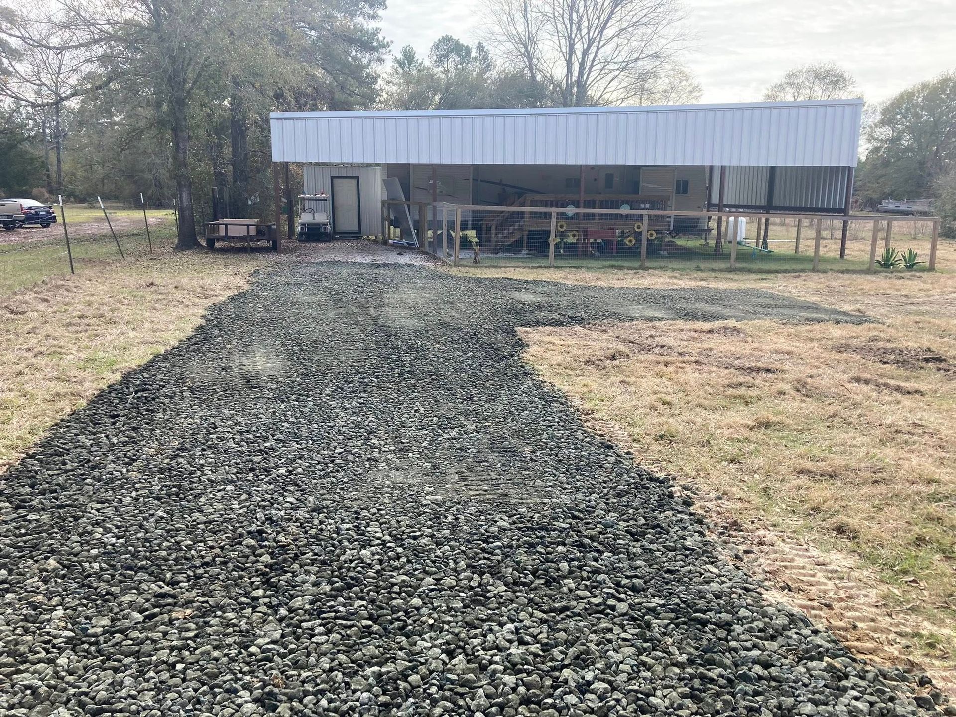 A gravel driveway leading to a house in a field.