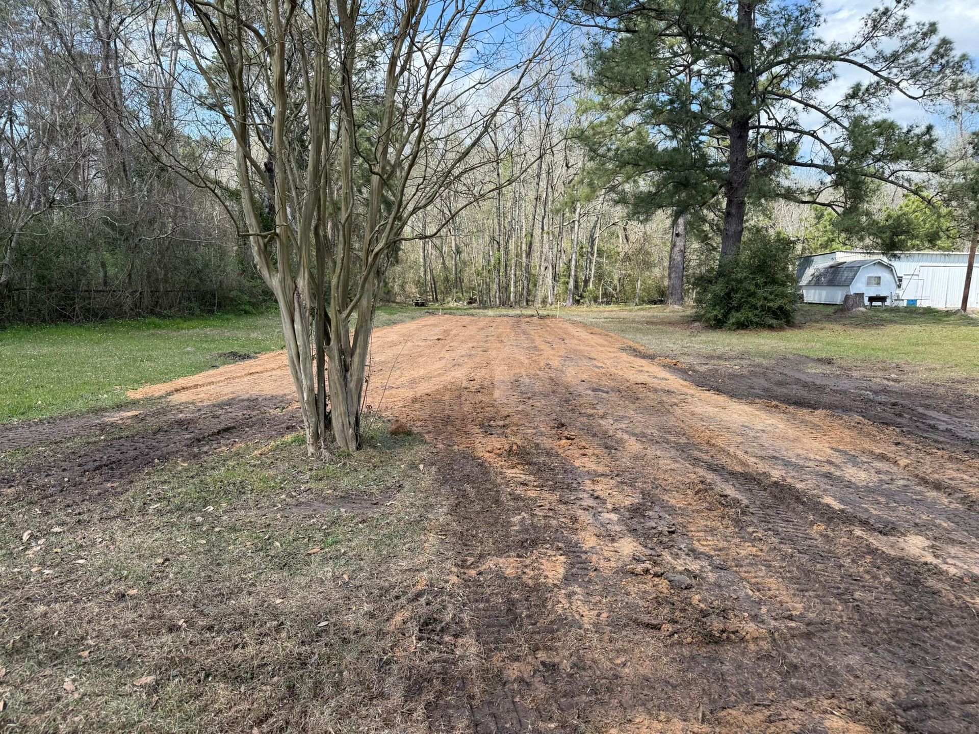 A dirt road going through a field with trees and a trailer in the background.