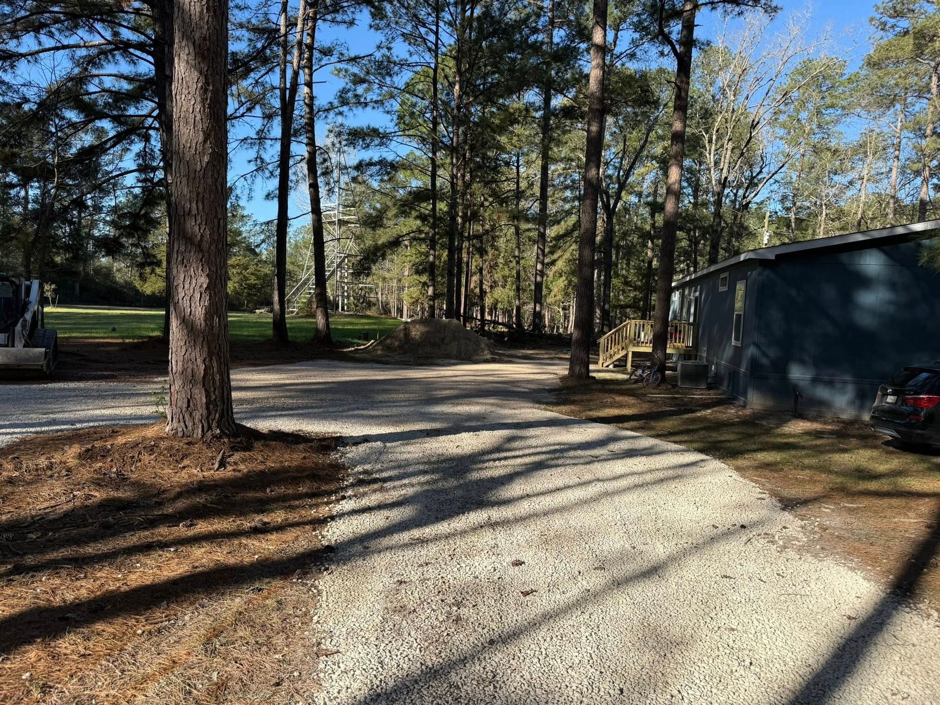 A car is parked on the side of a gravel road surrounded by trees.