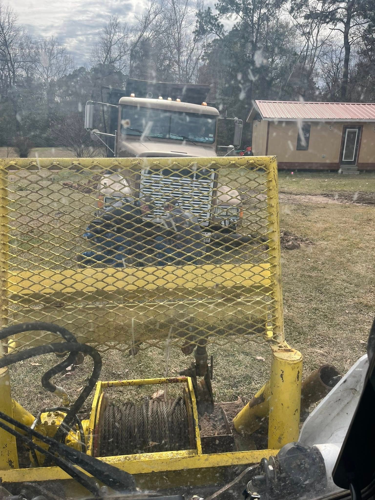A yellow truck is parked in a field with a house in the background.