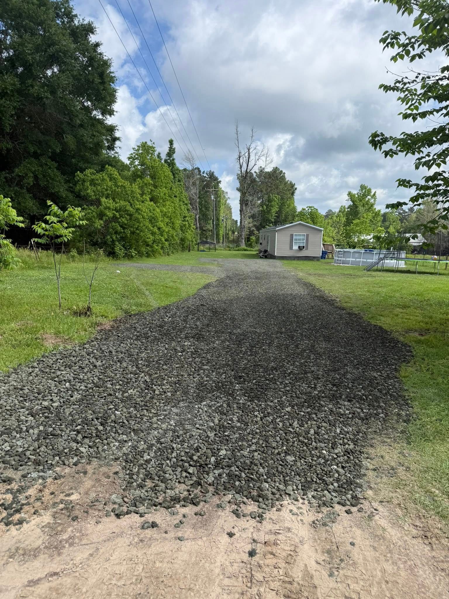 A gravel road leading to a house in the middle of a field.