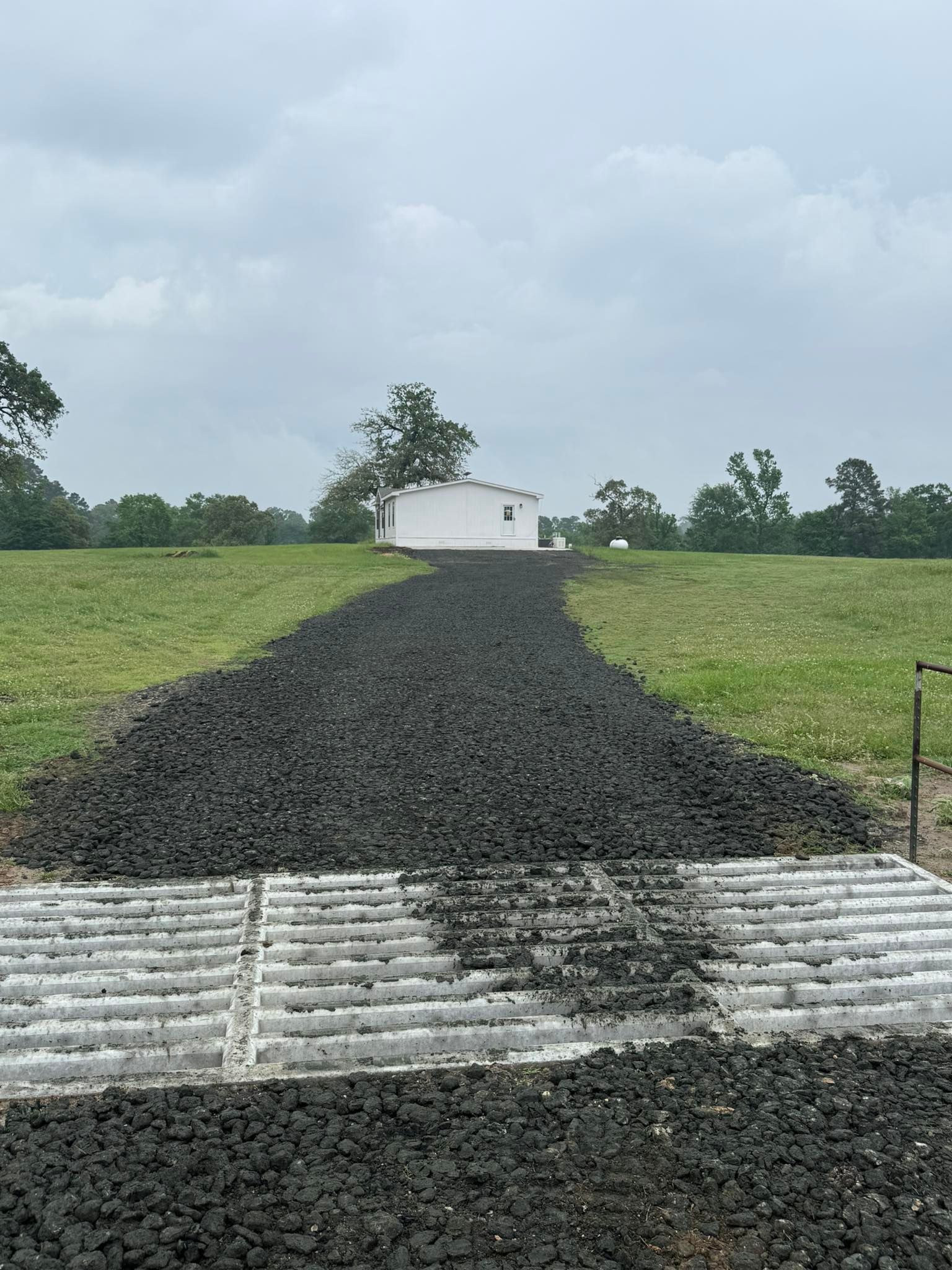 A dirt road going through a grassy field with a white building in the background.