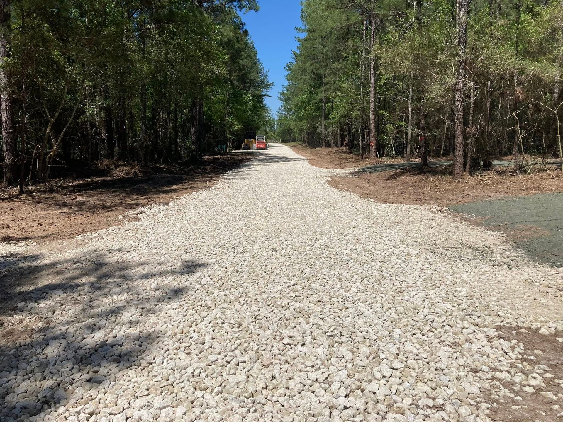A gravel road going through a forest with trees on both sides.