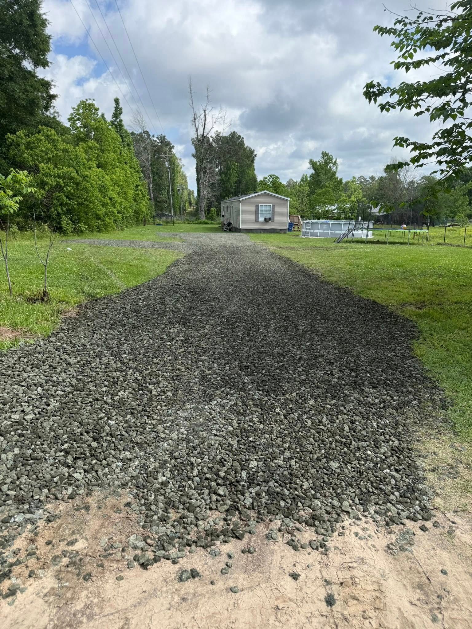 A gravel road going through a grassy field with a trailer in the background.