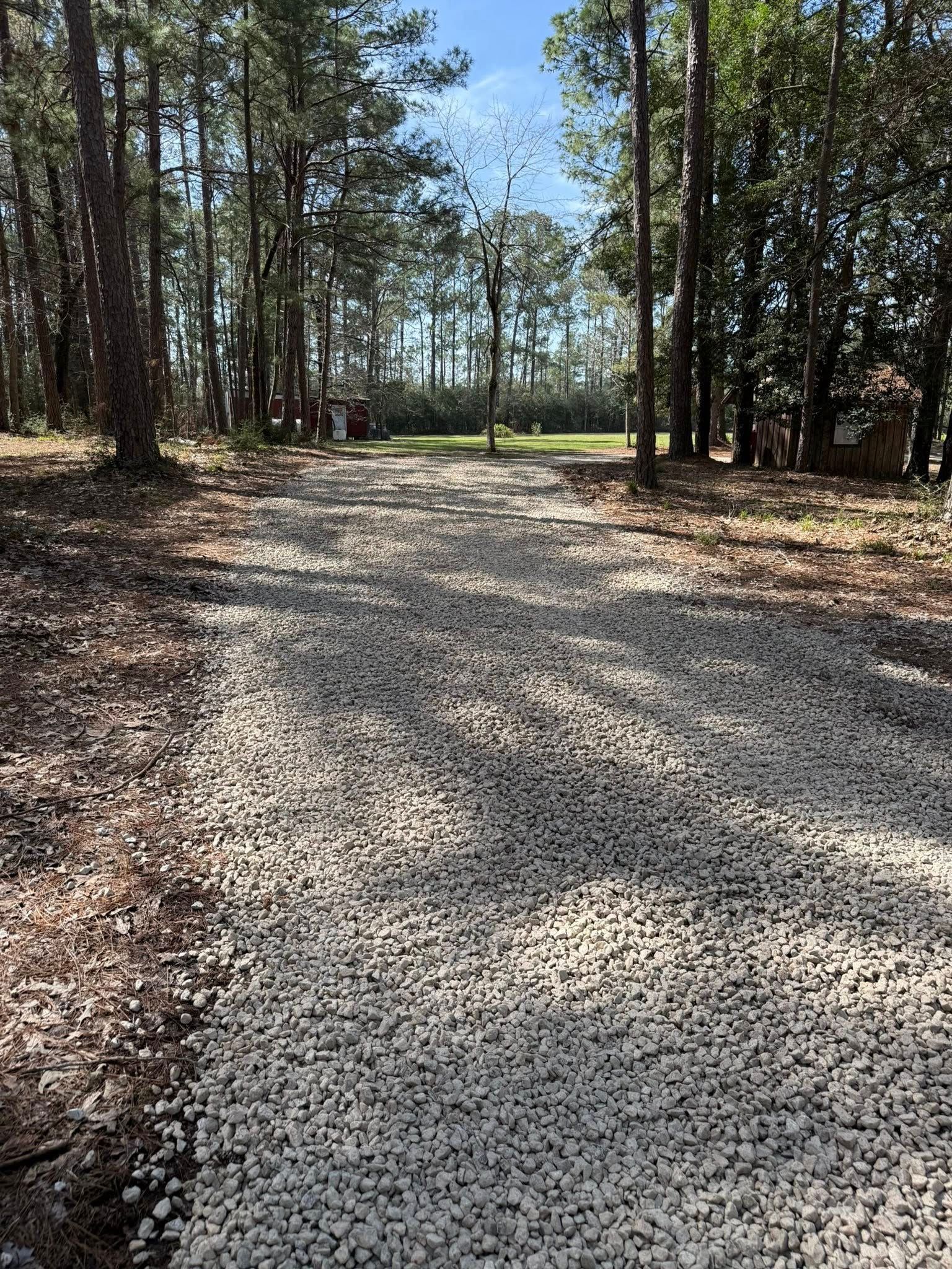 A gravel road going through a forest with trees on both sides.