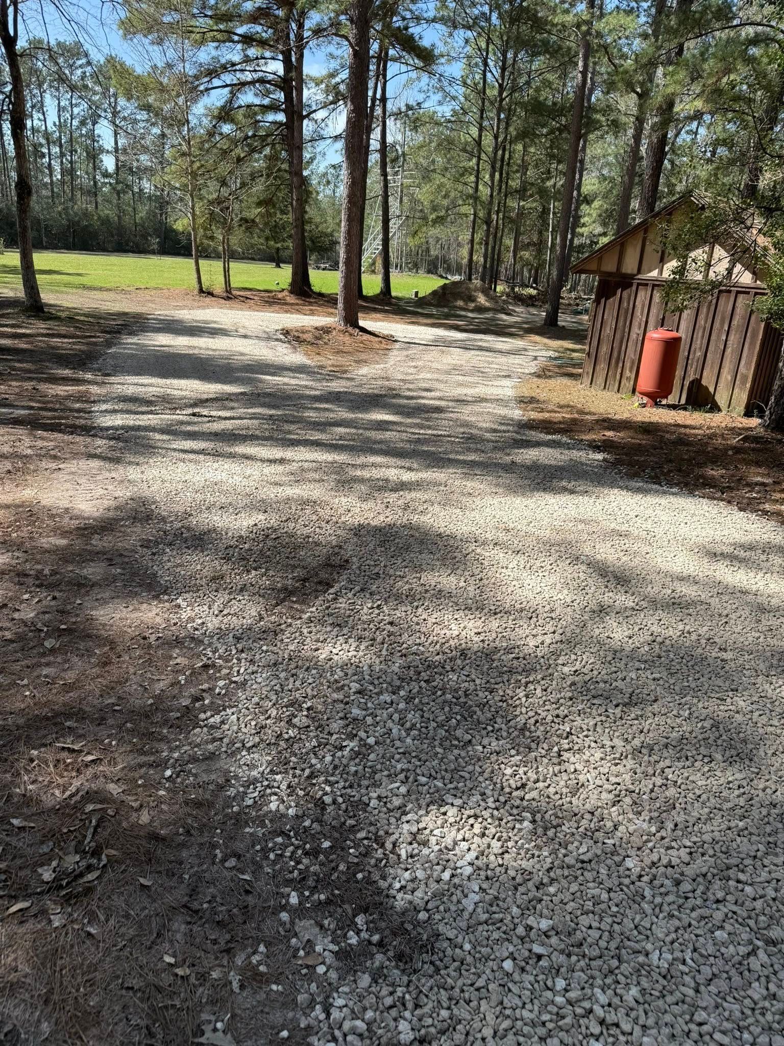 A gravel driveway leading to a house in the woods.