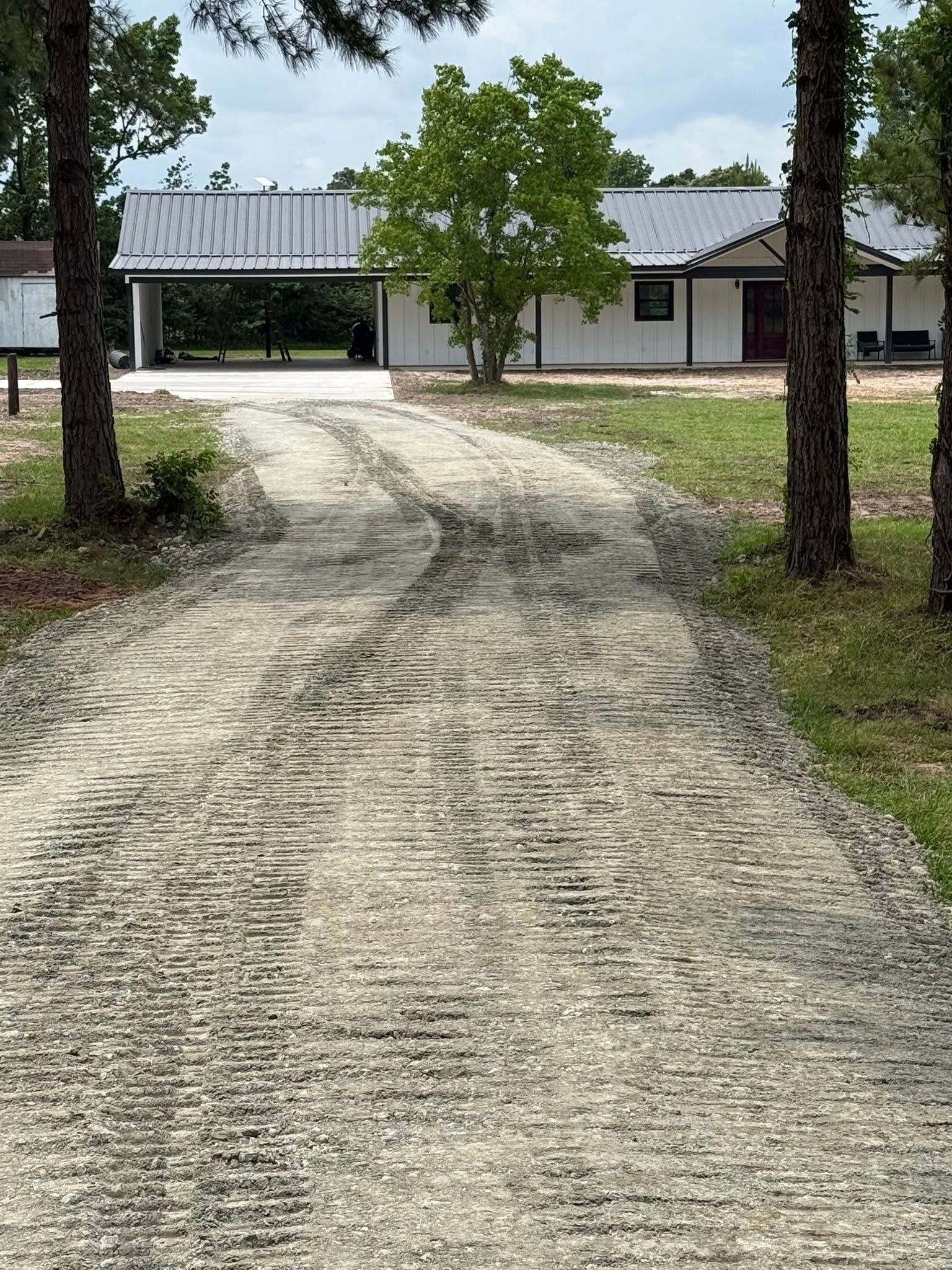 A dirt road leading to a house with trees on both sides.